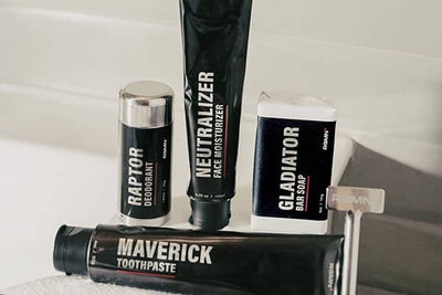 Collection of men's grooming products including deodorant, face moisturizer, toothpaste, and soap on a bathroom shelf.