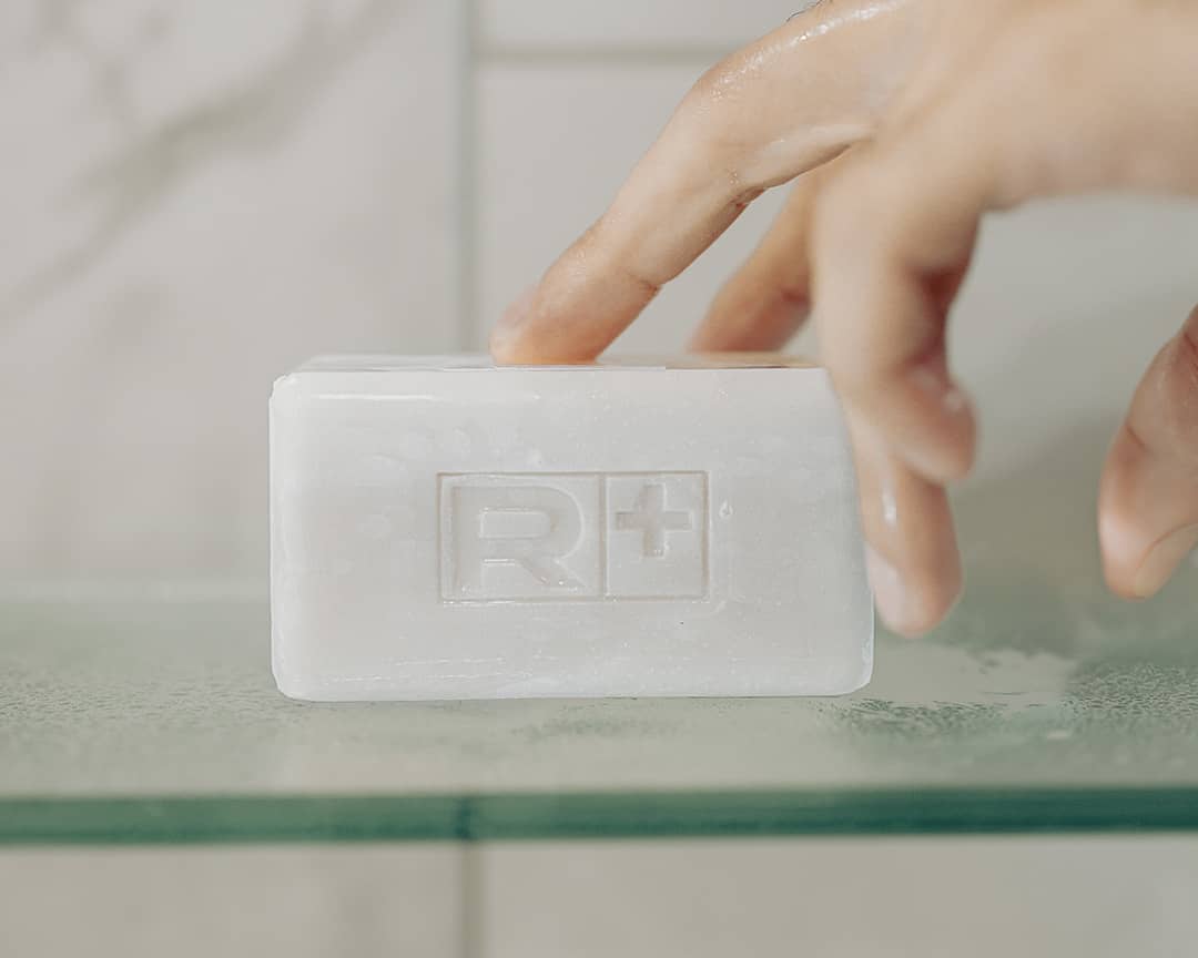 Bar of soap with RGMN+ logo held by a hand against a neutral background